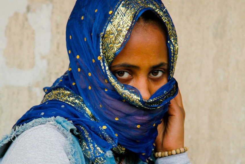 A woman in a blue and gold scarf wrapped around her face