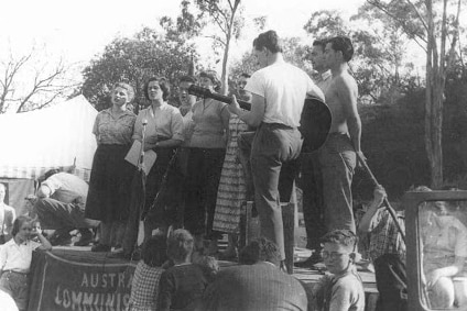 In a black and white photo, Salomea and a number of young people stand in front of a microphone on a small stage outside.