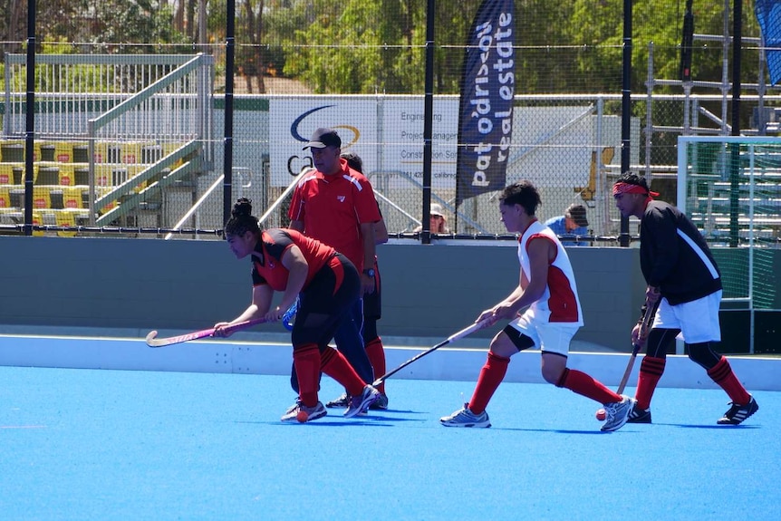 A hockey player hits the ball with the stick while other players stand behind her on the field.