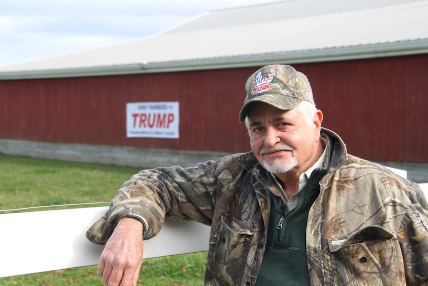 Dominic Marchese leans on a fence in front of his barn, which carries a campaign sign for Donald Trump.