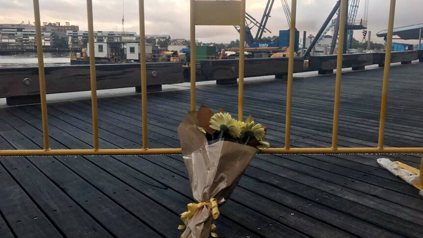 A bunch of flowers lean against a fence, with a crane barge visible behind.