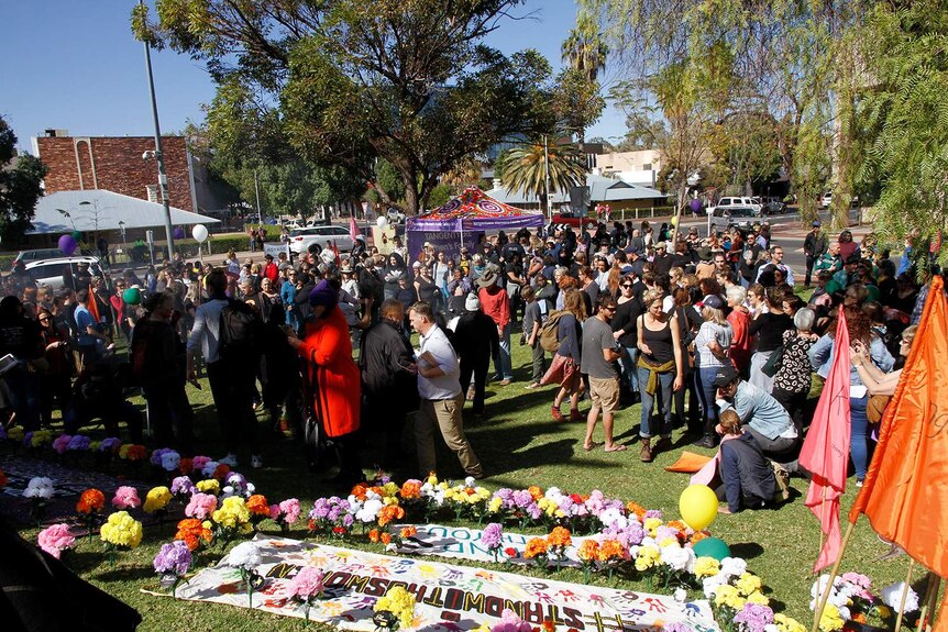 People mill around flowers and banners on the ground in Alice Springs