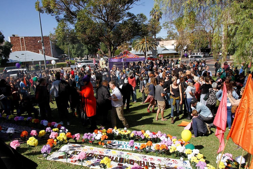 People mill around flowers and banners on the ground in Alice Springs