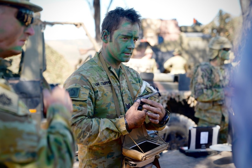 An Australian soldier in battle dress holds a small black hornet drone in his hand