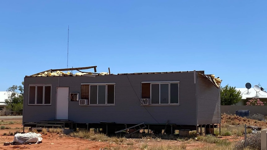 A wide shot of a grey house in red dirt