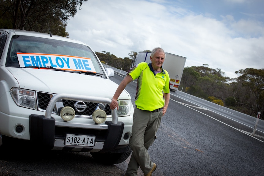 Garry Wilson stands next to his vehicle with a sign that says 'employ me' at a truck stuck along the Sturt Highway.