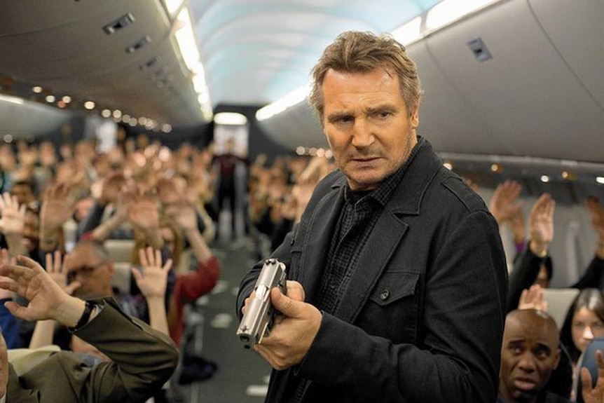 Liam Neeson brandishing a gun in the aisle of a plane.