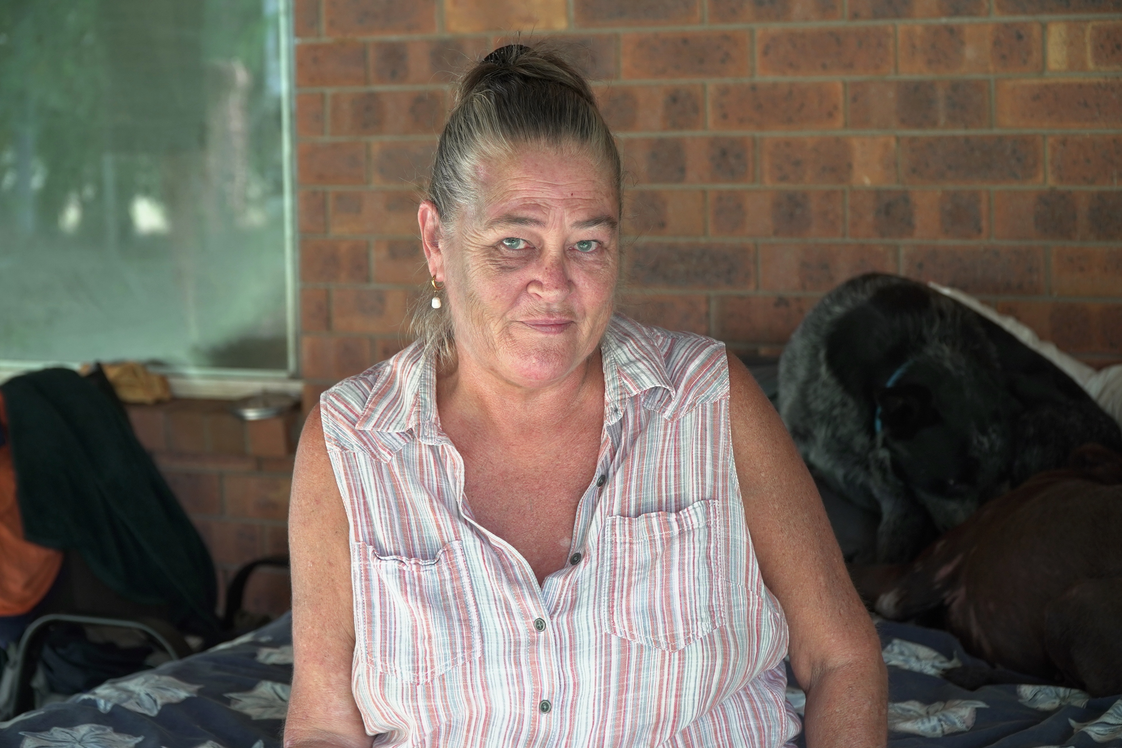 A woman in a striped, sleeveless shirt looks at the camera.