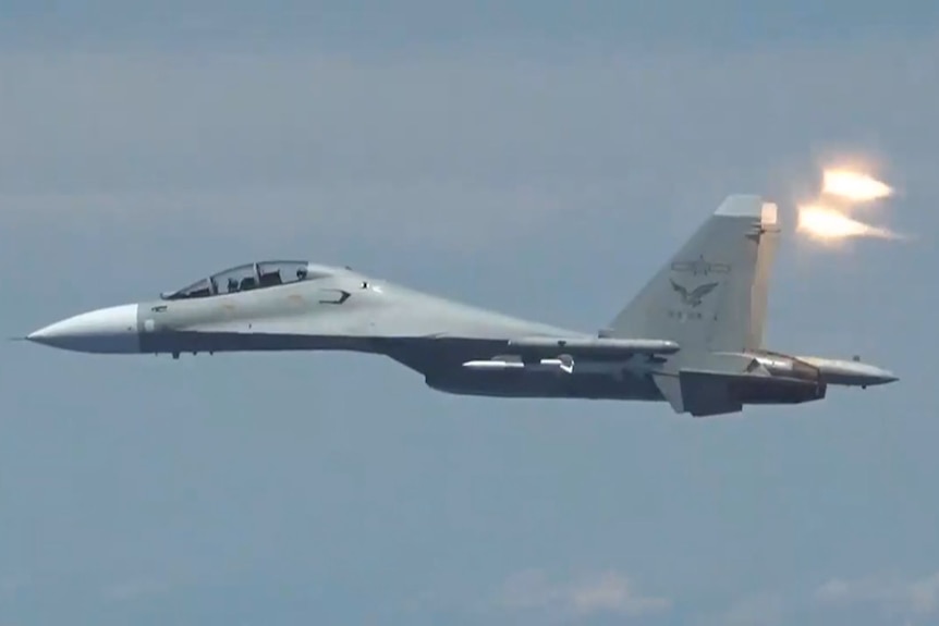 A fighter jet releases two bright flares as it flies in the air.