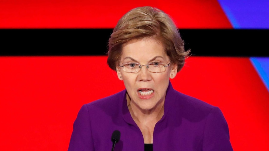 Elizabeth Warren holds her hands up as she speaks in front of a red and blue background