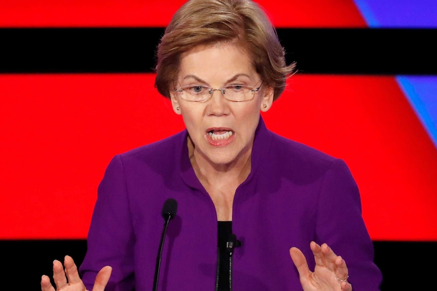 Elizabeth Warren holds her hands up as she speaks in front of a red and blue background