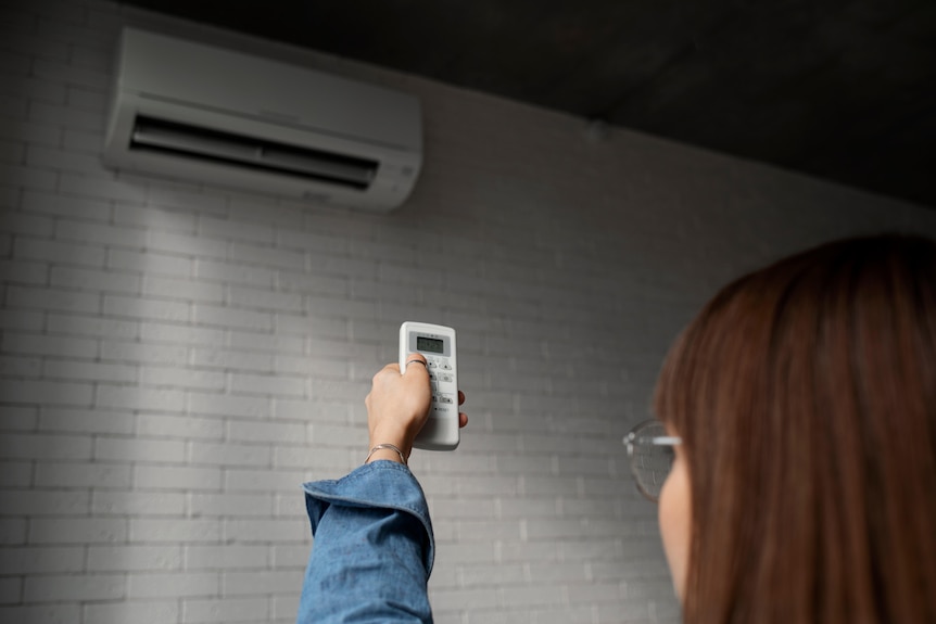 A lady holding an aircon remote control and pointing it towards the unit system on the wall