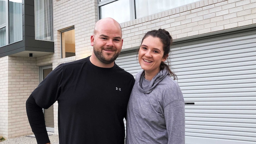 A man and woman stand outside their two storey house.