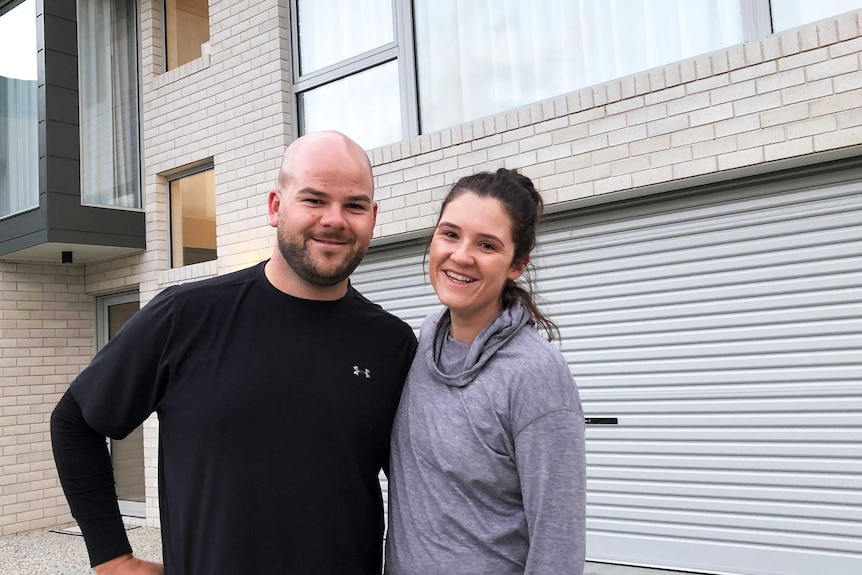 A man and woman stand outside their two storey house.