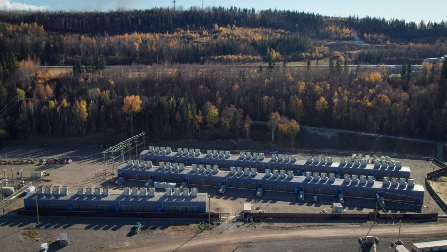 A bird's eye view of three long sheds in an isolated stretch of land on the side of a hill.