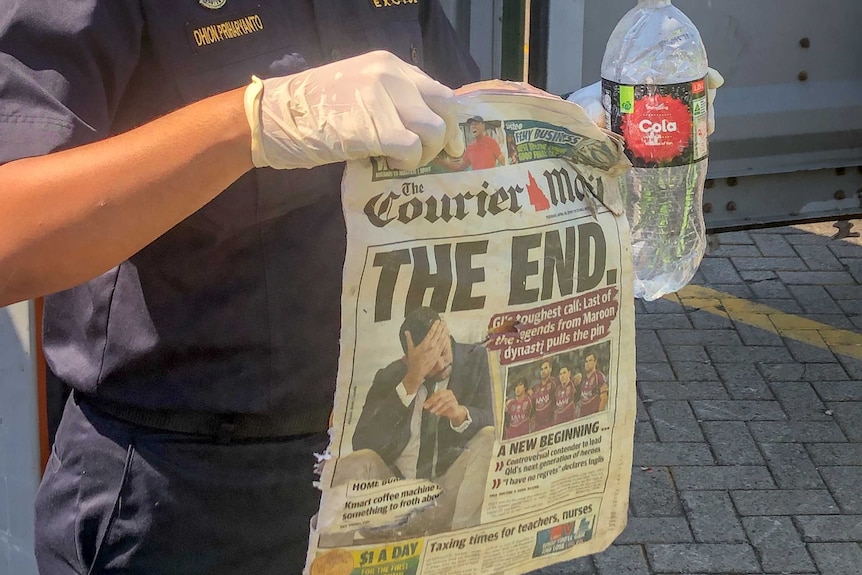 A man in a mask holds up a copy of the Courier Mail newspaper