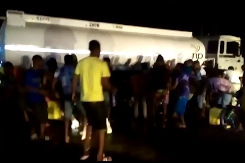 People stand around a fuel tanker at night.