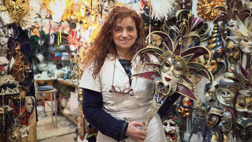 A woman stands holding an artisan face mask.