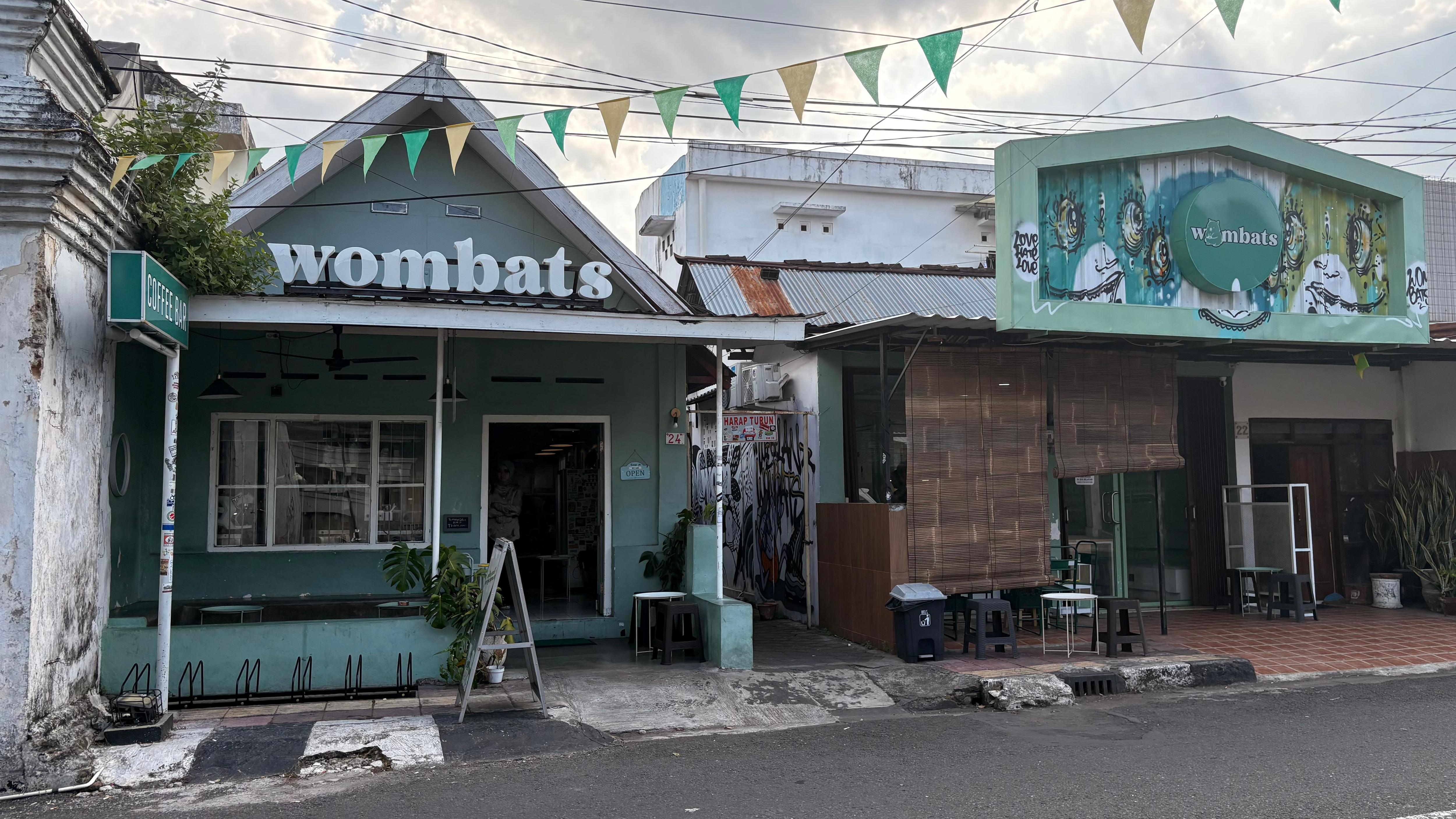 Una casa verde con el nombre de Wombat en el techo y dos personas sentadas.