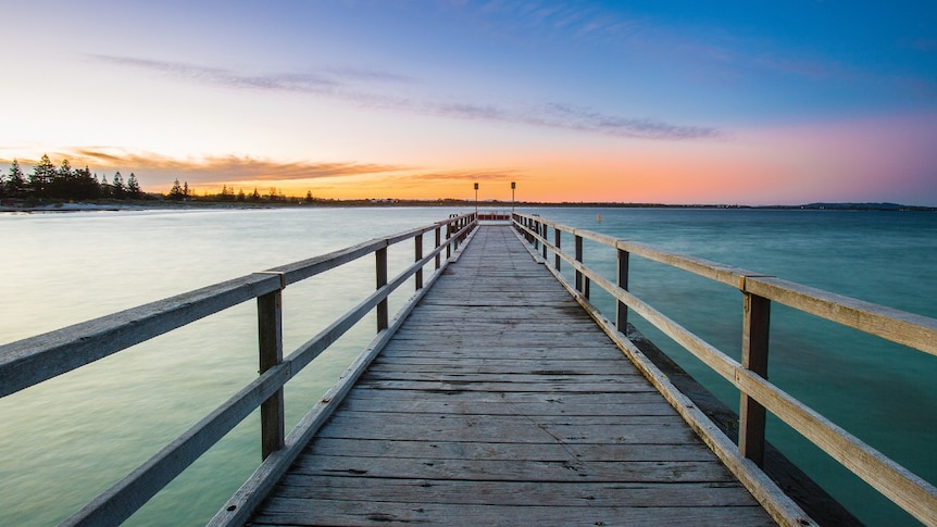 A jetty over the ocean with a yellow sunset on the horizon.