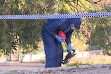 A forensics officer in a blue body suit and gloves bends over while carrying some markers. 