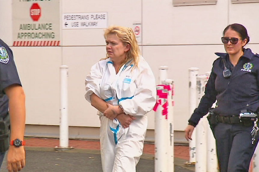 A woman in a prison suit walks between two officers.