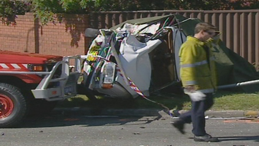 An emergency worker walks past the white sedan which was turned on its side in the fatal crash at Wilson