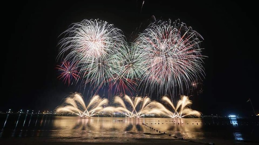 numerous gold, purple and green fireworks being fired into the air and off the ground at night