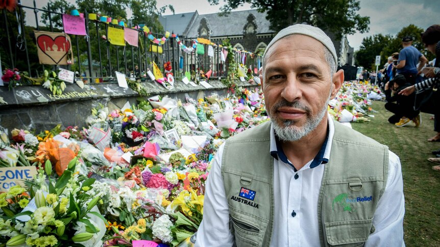 A man sits in front of a wall of flowers.