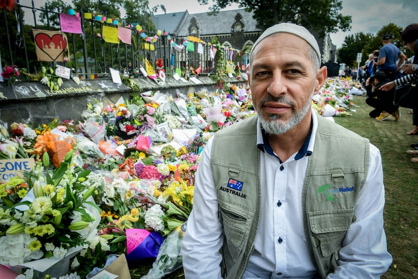 A man sits in front of a wall of flowers.