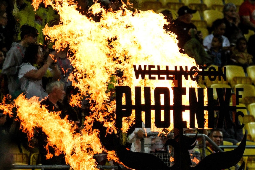 A Wellington Phoenix sign is surrounded by flames ahead of an A-League football match