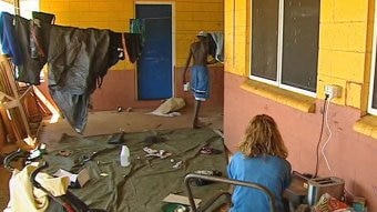 Two Aboriginal people walking and sitting in overcrowded housing.