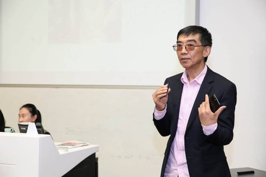 Wang Zhengliang standing while wearing a pink shirt and suit jacket.