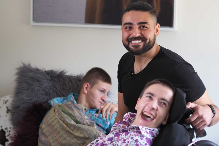 A man smiling at the camera while sitting beside two disabled men