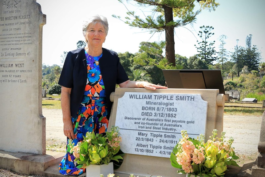 Lynette Silver kneels by William Tipple Smith's headstone with her hand resting on it.