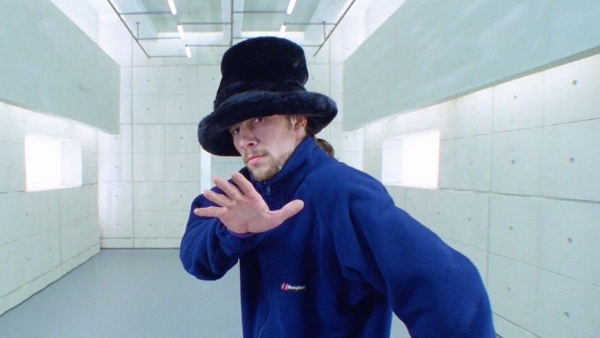 Jamiroquai's Jay Kay holds his hand to the camera in the video for Virtual Insanity. He wears a plush top hat and blue jacket