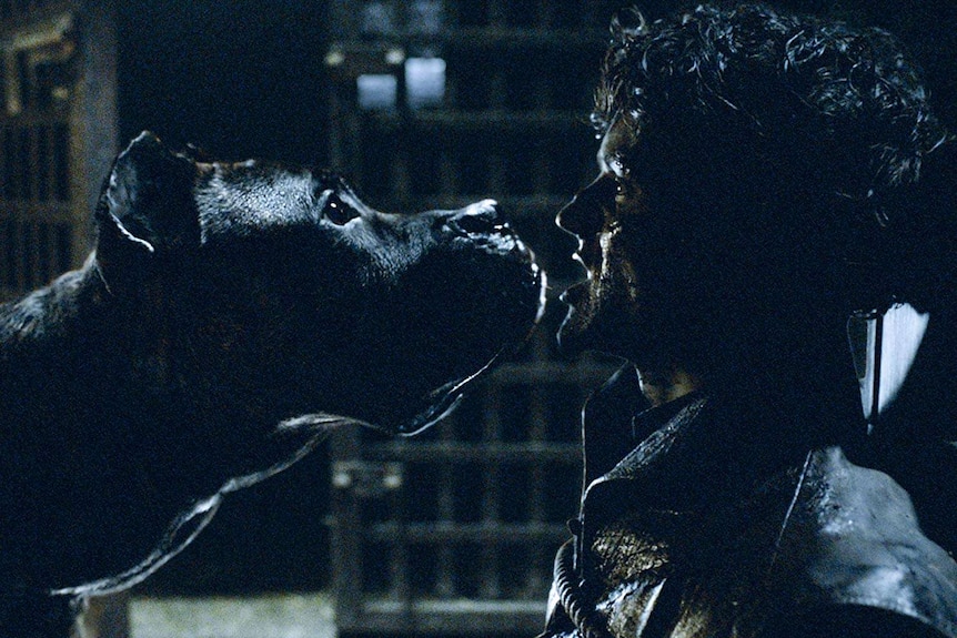 A man is shackled and injured while a dog prepares to eat him in an image taken from a fantasy tv show