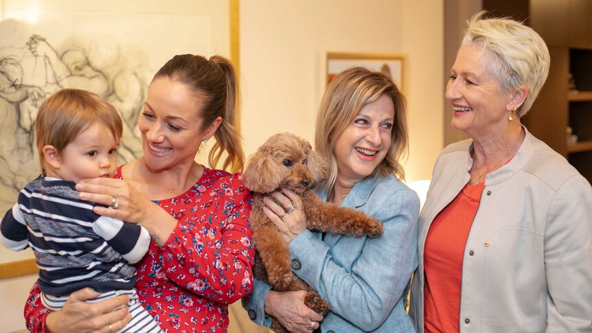 Three women and a toddler are all smiles while holding a small brown dog