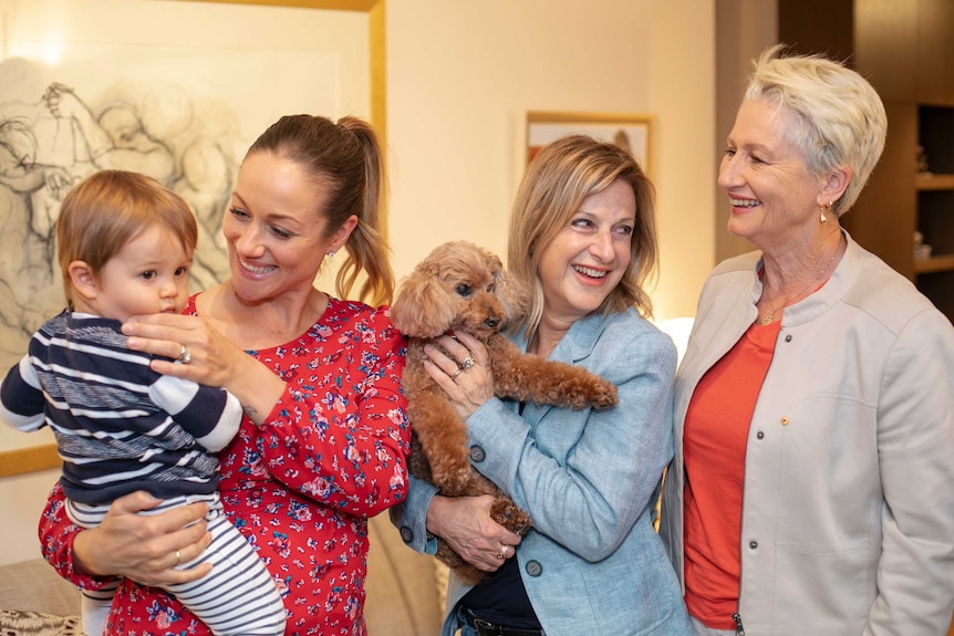 Three women and a toddler are all smiles while holding a small brown dog