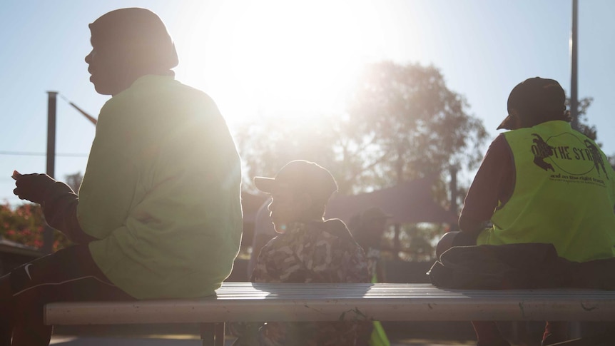 Three young people sitting on a picnic table with their backs to the camera