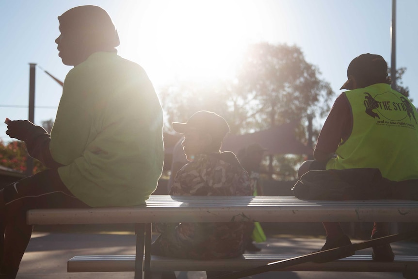 Three young people sitting on a picnic table with their backs to the camera