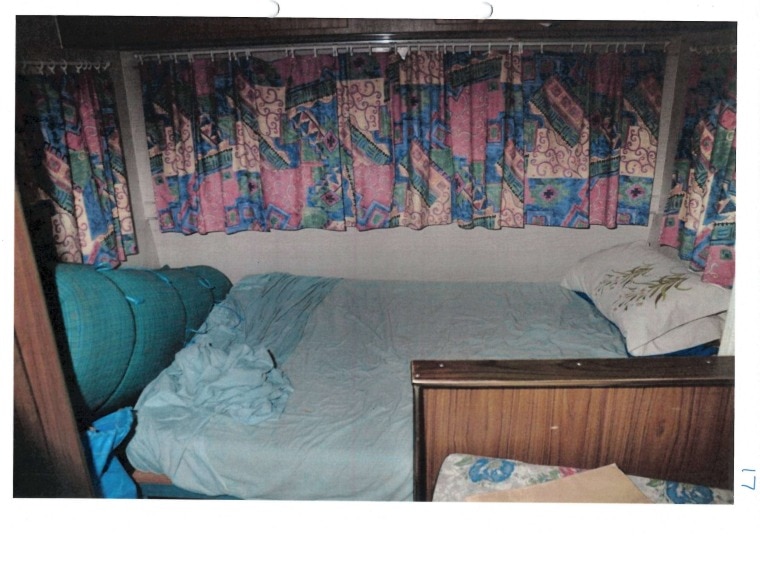 The interior of a caravan, shows a bed with walls around it and patterned curtains.