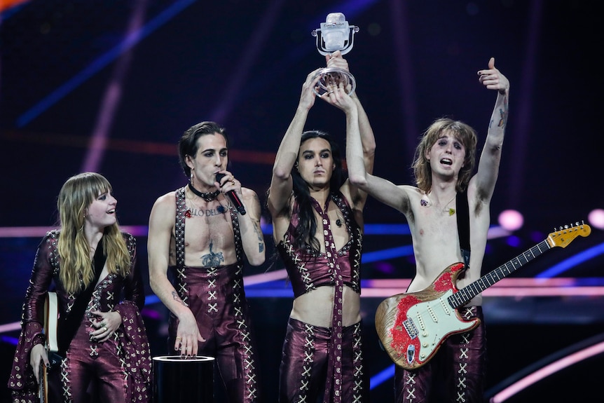 A happy Italian rock group stand on stage with one holding the trophy after the end of the Eurovision Song Contest.