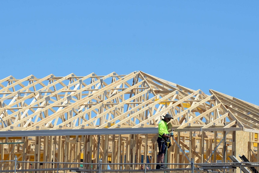 A carpenter works on a home under construction with a blue sky above.