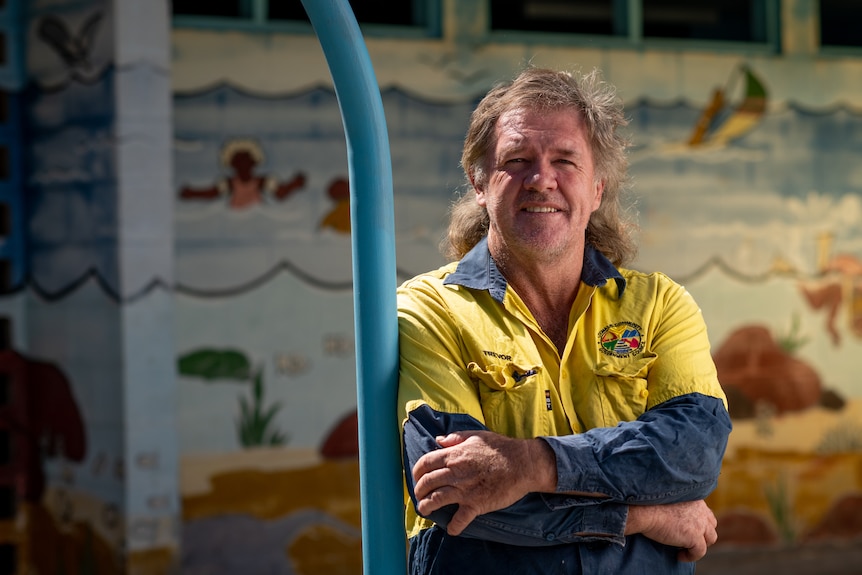 A man in high vis smiling and crossing his arms in front of a wall featuring a colourful mural.