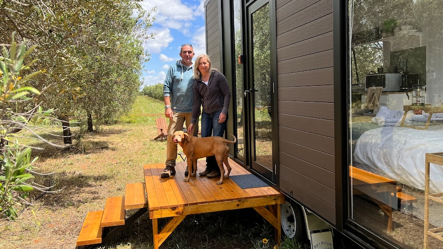 Gary and Isabel sand on the front deck of their tiny house which can be booked for a holiday