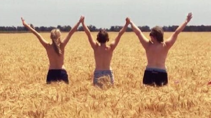 Three young grain growers stand in a big crop of wheat at Gulargambone in NSW, arms raised, naked to their waist, celebrating.