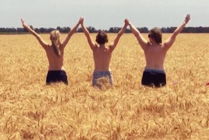 Three young grain growers stand in a big crop of wheat at Gulargambone in NSW, arms raised, naked to their waist,