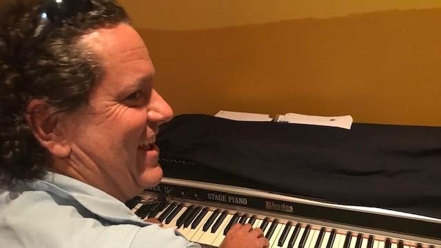 A smiling man plays piano