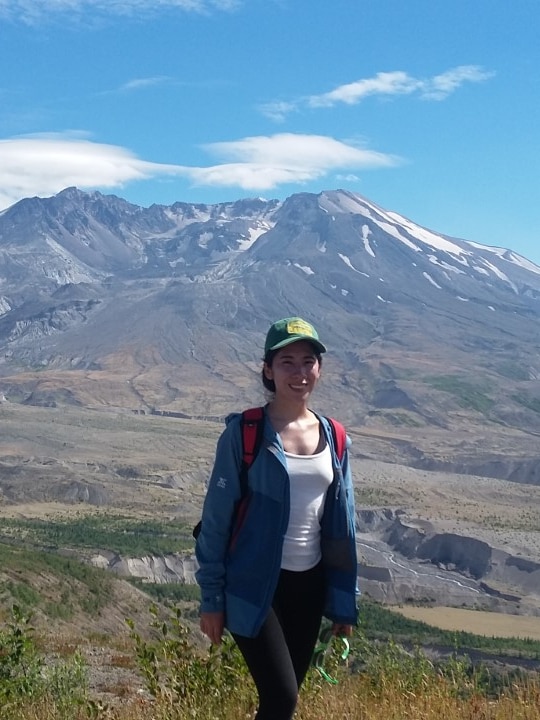 Mujer vestida de senderismo con un volcán a lo lejos.